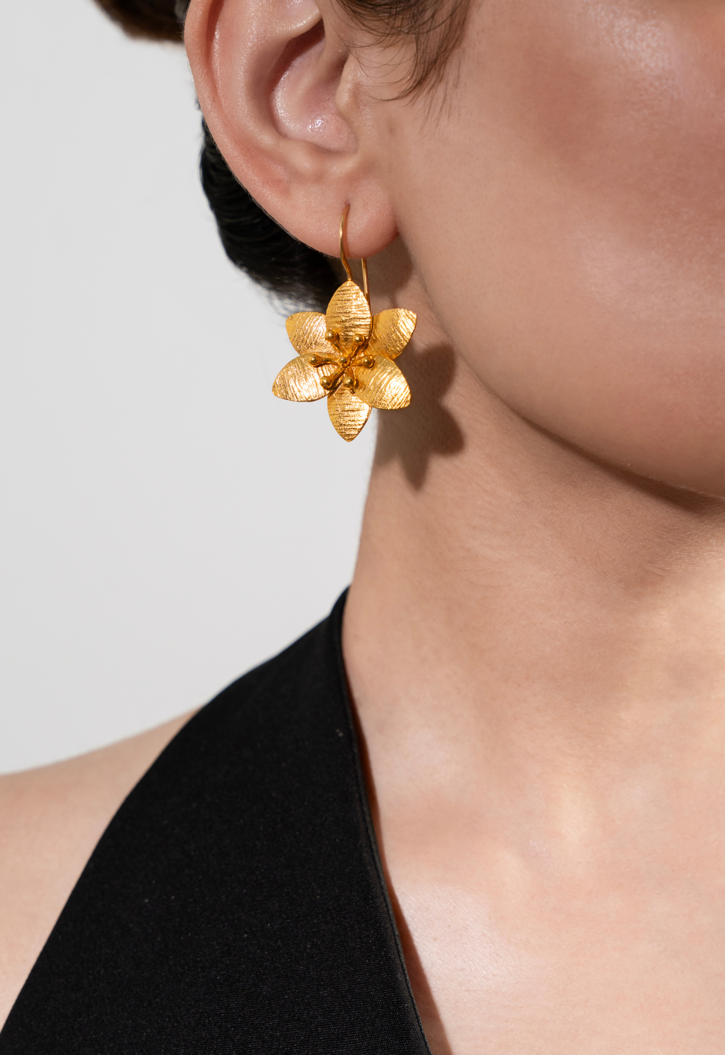 Gold flower-shaped earring worn by a person against a neutral background