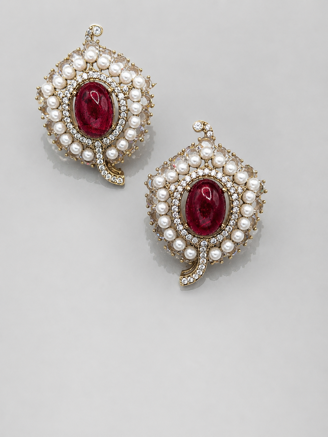 Pair of earrings with red gemstones and pearl-like accents on a light gray background