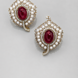 Pair of earrings with red gemstones and pearl-like accents on a light gray background