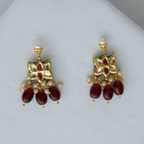 Pair of gold earrings with red gemstones on a light gray background

