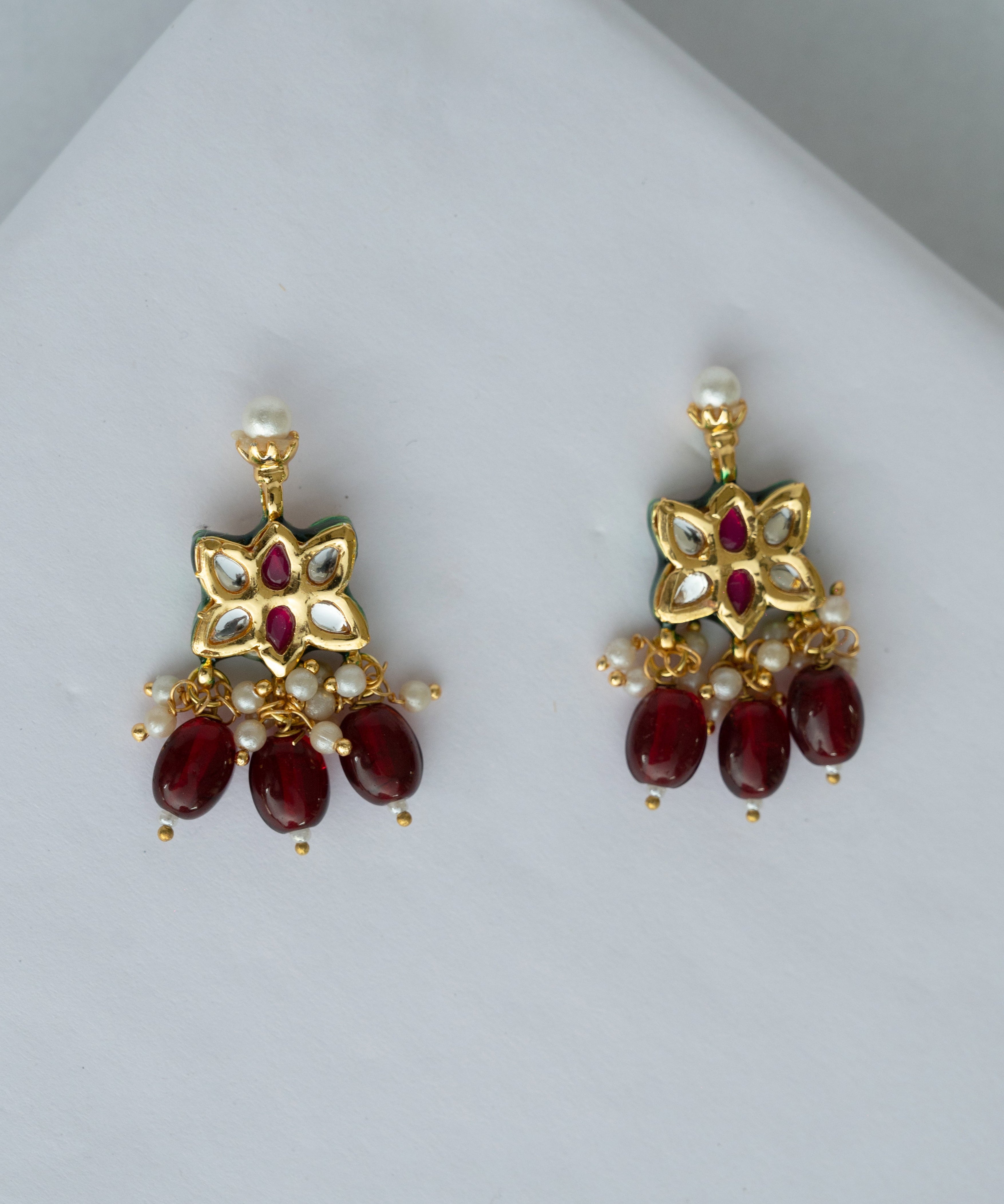 Pair of gold earrings with red gemstones on a light gray background


