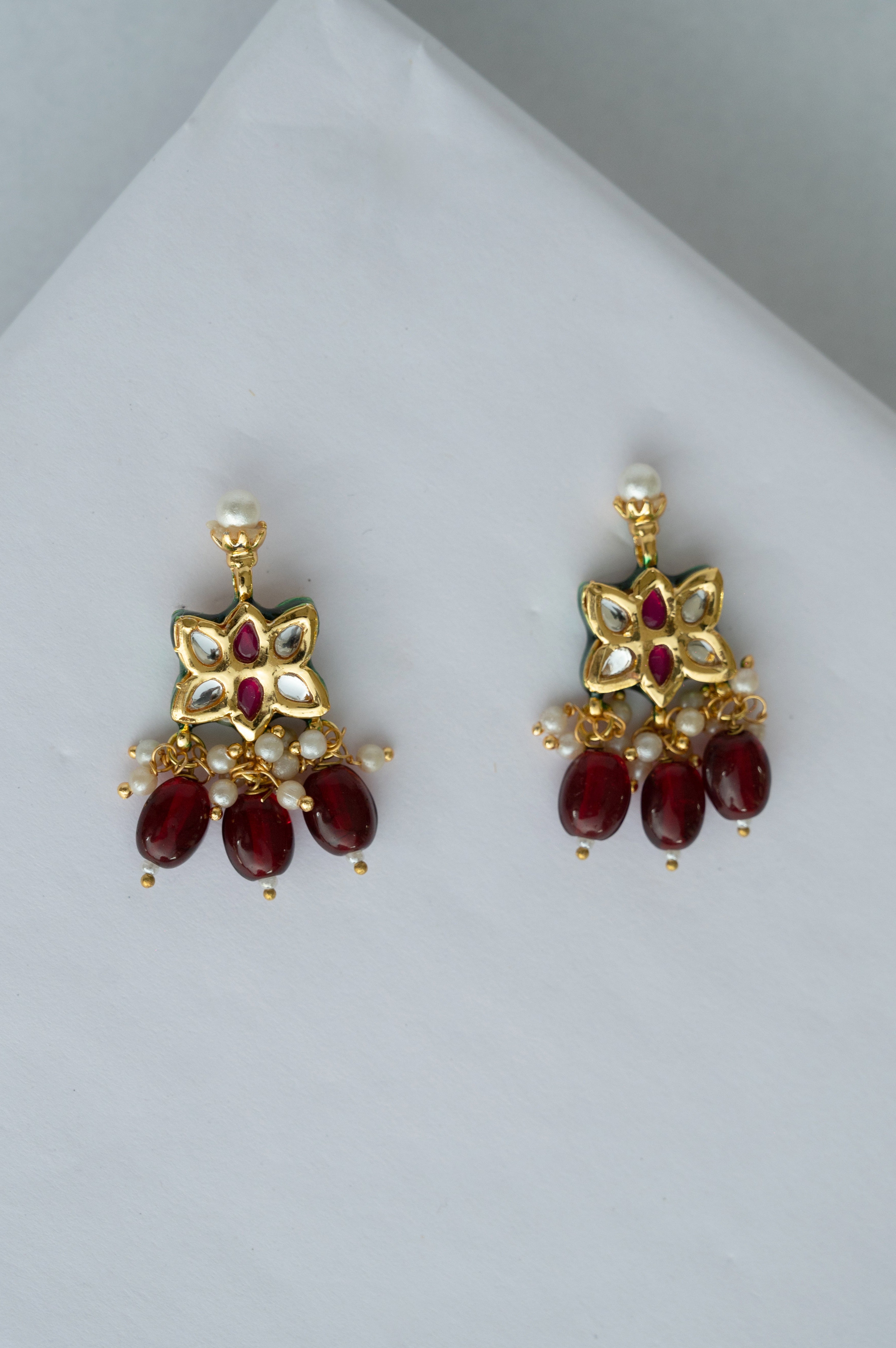Pair of gold earrings with red gemstones on a light gray background

