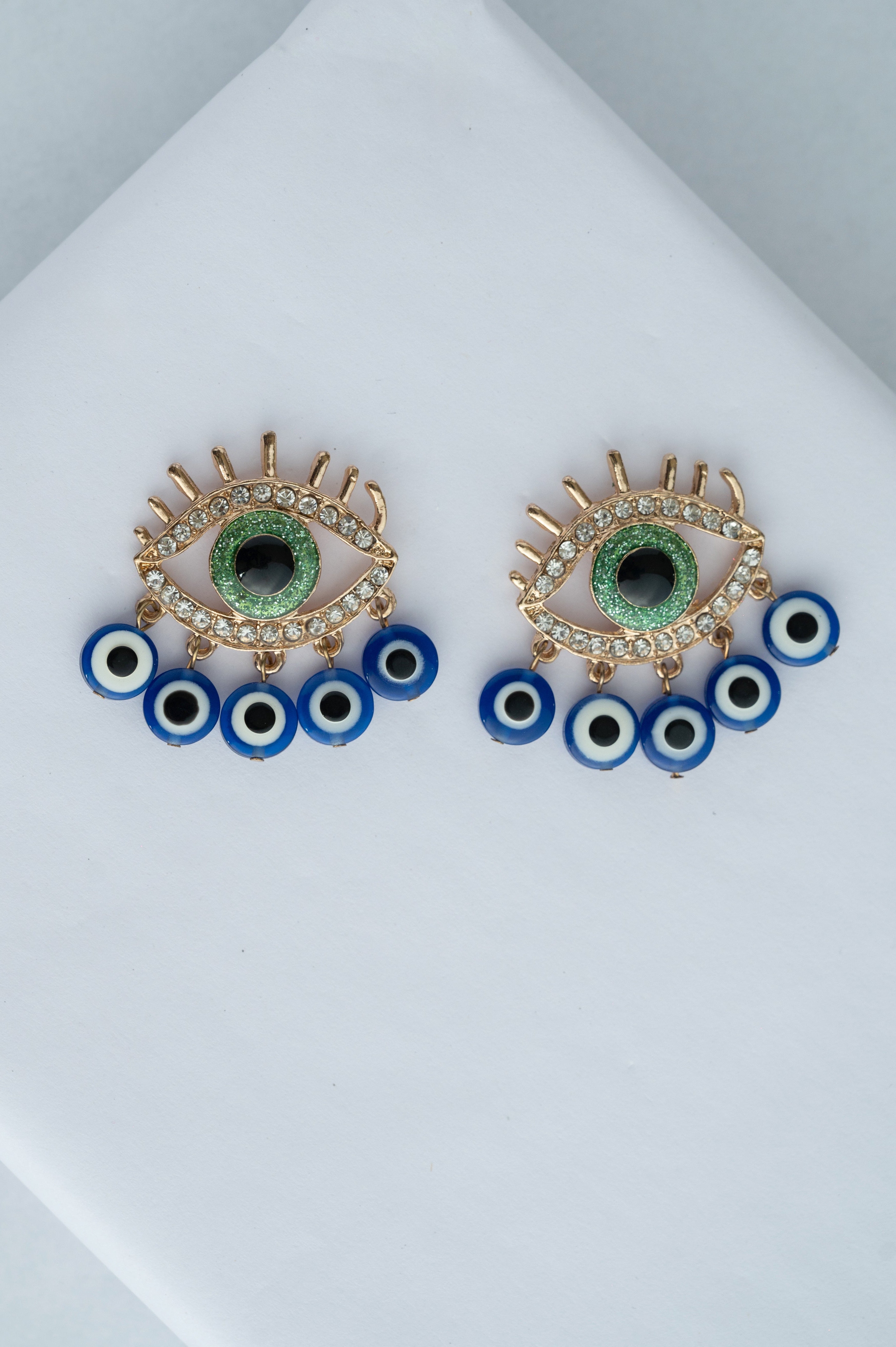 Pair of eye-shaped earrings with green centers and blue and black accents on a white surface.