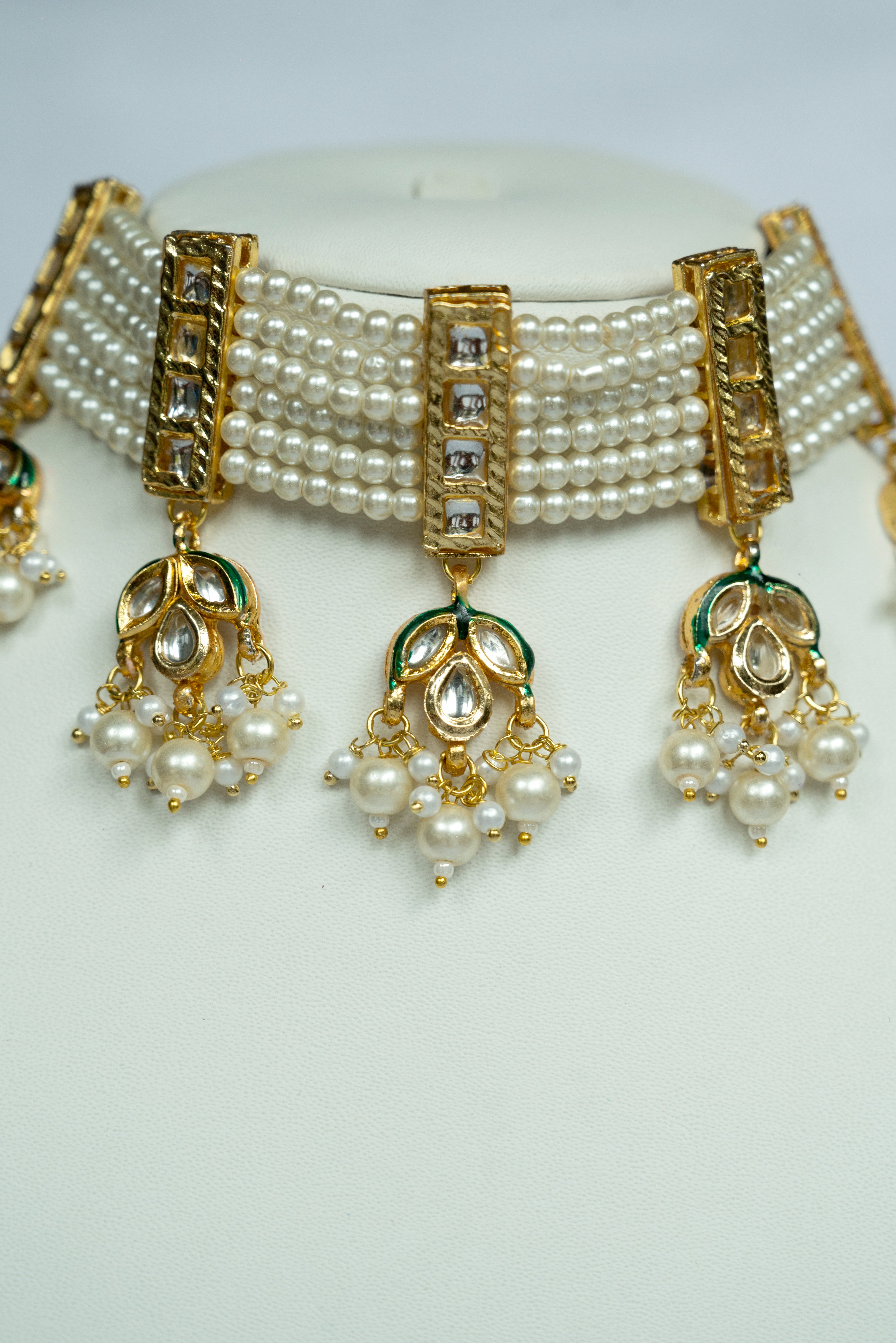 Pearl necklace with gold and green accents on a white background