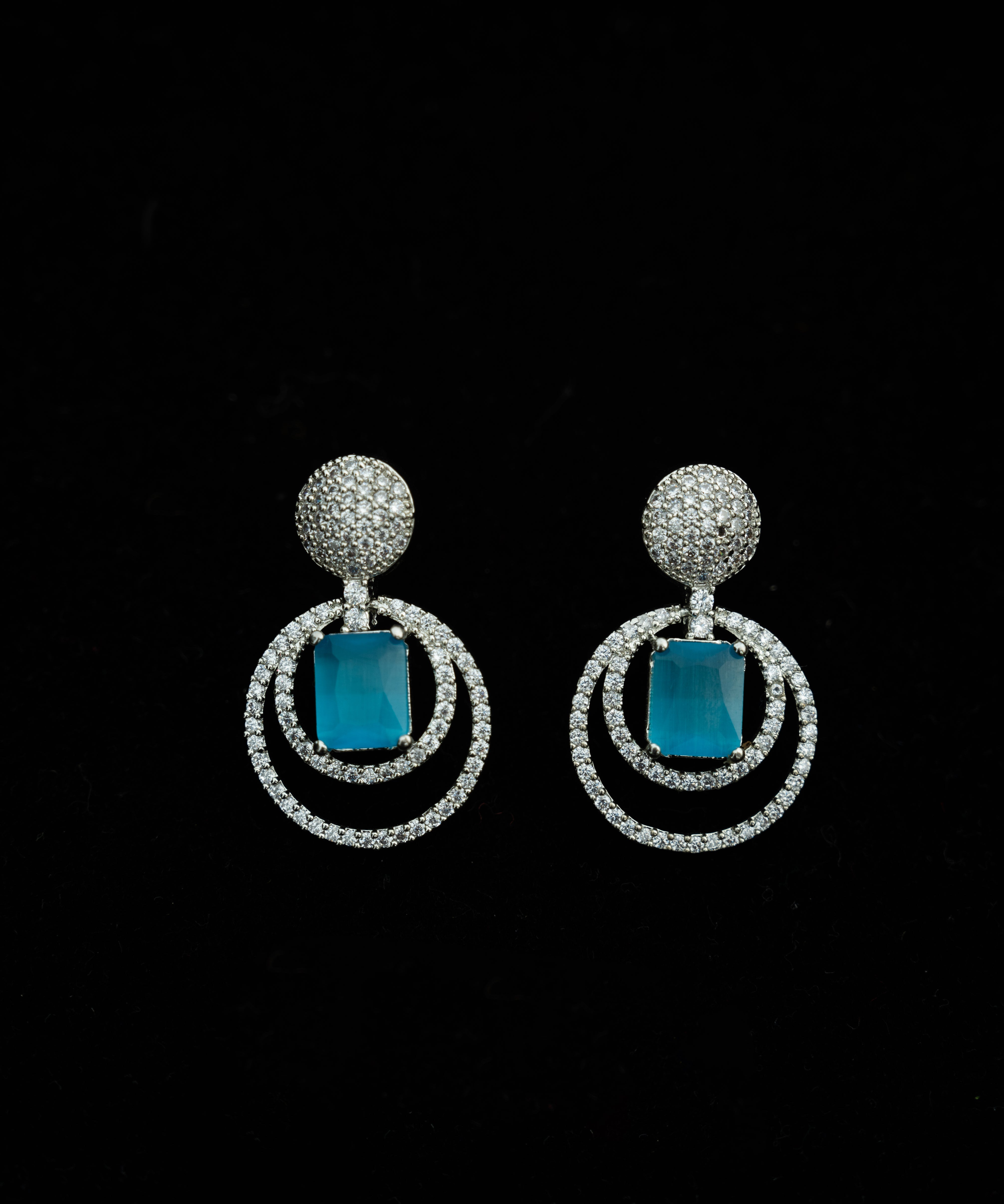 Pair of earrings with blue stones and silver circular designs on a black background


