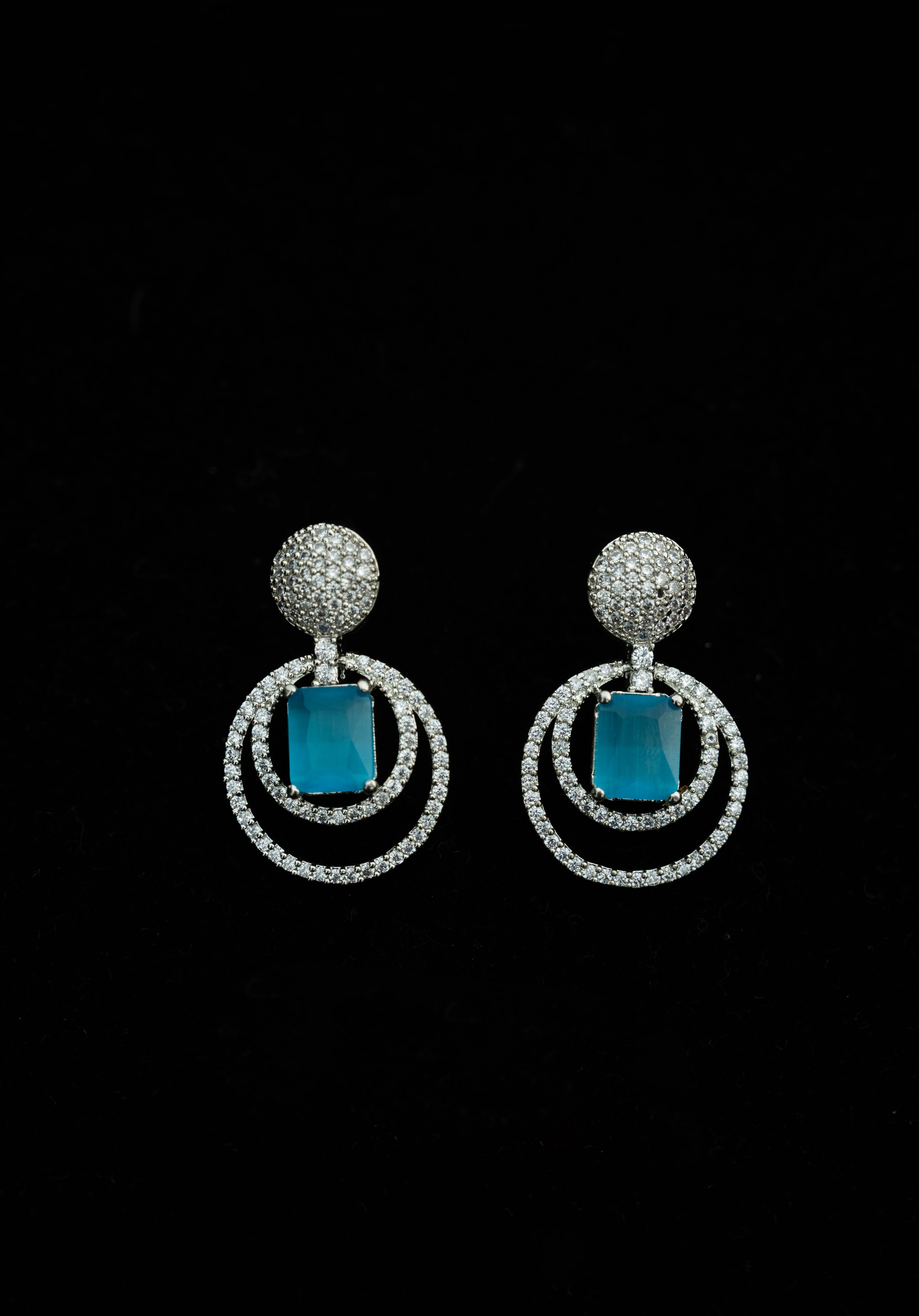 Pair of earrings with blue stones and silver circular designs on a black background

