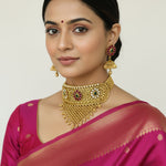 Woman wearing traditional jewelry and a pink saree against a plain background

